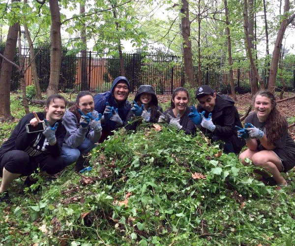 A group of seven high school kids crouching around a pile of invasive plants they removed.